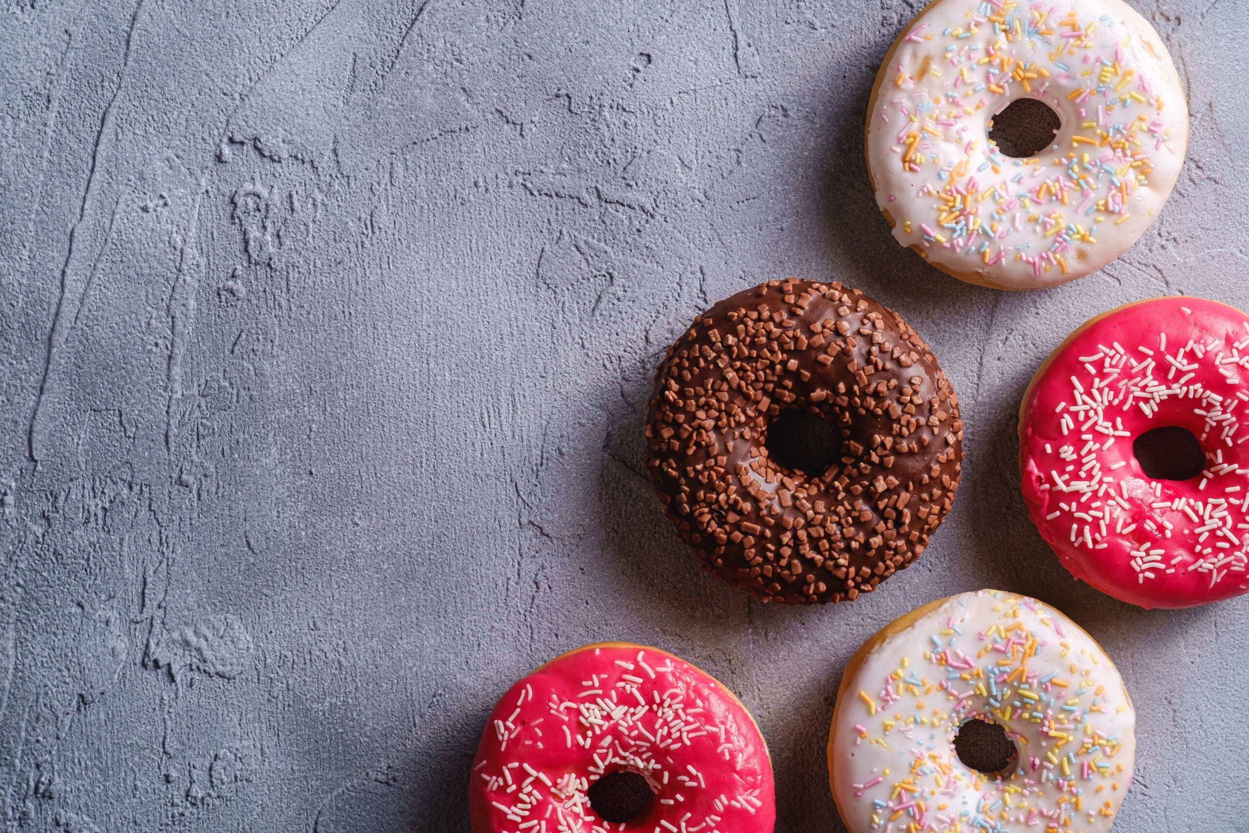 An artistic arrangement of colorful donuts with sprinkles on a textured gray background.